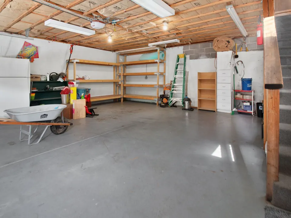 Garage with wooden shelving units along the back wall, a wheelbarrow and a ladder on a clean concrete floor