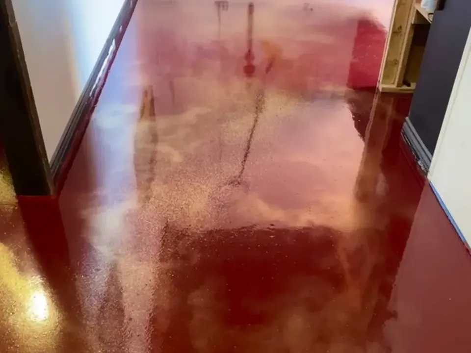 Glossy deep red floor with swirls of gold shimmer in a narrow room with white walls and a wooden shelf unit.